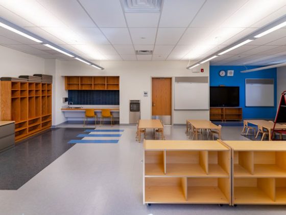 The interior of a preschool classroom with tables, chairs, and cubby-hole cabinets.