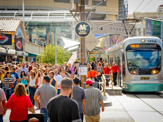 Large groups of people in downtown Phoenix with a Valley Metro light rail train in the background.