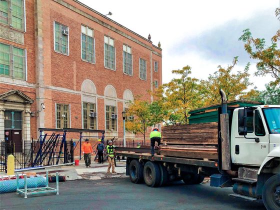 Exterior view of construction vehicle in front of red brick school building.