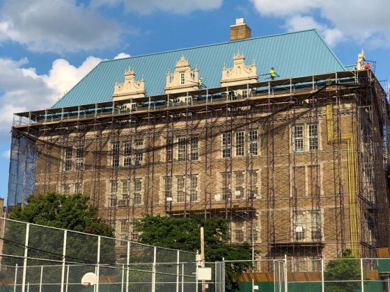 Scaffolding and protective netting cover the exterior of a historic school building in New York City.