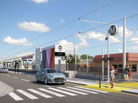 Woman waiting to cross street near East San Fernando Valley LRT station as gray car passes in street