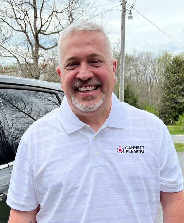 A man with gray hair and a beard wearing a white shirt smiling for the camera.