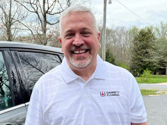 A man with gray hair and a beard wearing a white shirt smiling for the camera.