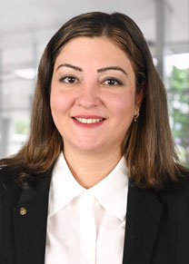 A women with brown hair wearing a white blouse and black jacket smiling for the camera.