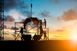 Silhouette of construction workers building a recycling icon with the sunset in the background.