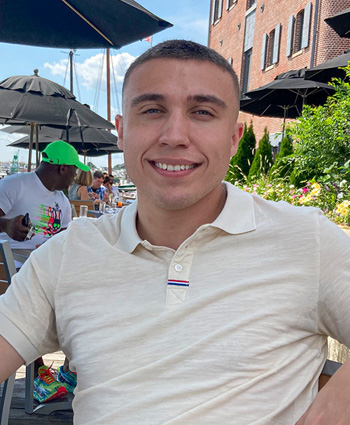 Certified Depreciation Professional Jason Powery smiles while wearing a yellow polo shirt and sitting at a table outside at the Inner Harbor in Baltimore, Maryland.