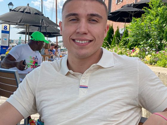 Certified Depreciation Professional Jason Powery smiles while wearing a yellow polo shirt and sitting at a table outside at the Inner Harbor in Baltimore, Maryland.