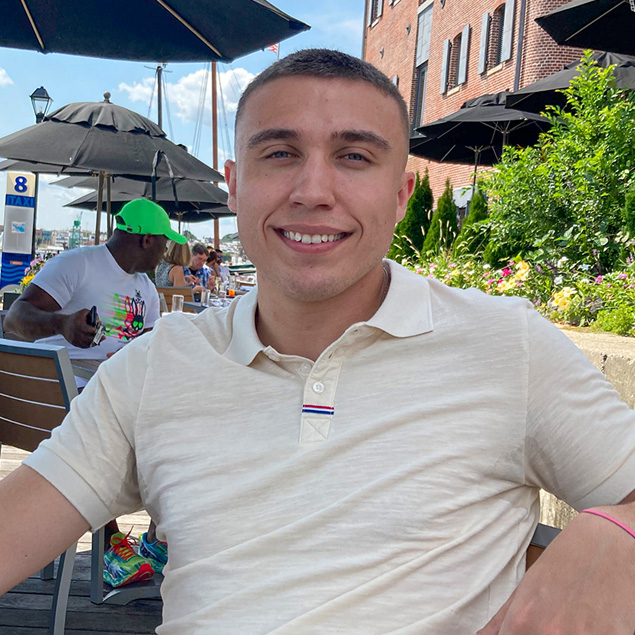 Certified Depreciation Professional Jason Powery smiles while wearing a yellow polo shirt and sitting at a table outside at the Inner Harbor in Baltimore, Maryland.