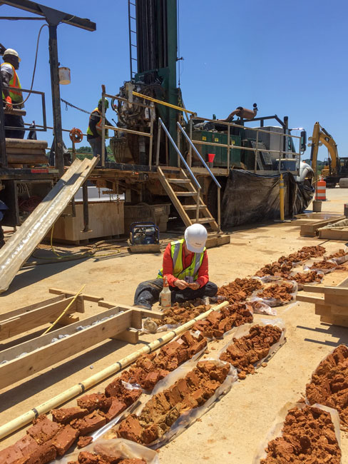 Engineer sitting on the ground in front of rows of soil boring samples.