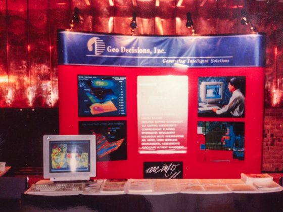 GeoDecisions’ carpet wrapped table-top booth display at an industry conference in the 1990s. On the table are also an old computer displaying maps and multiple brochure handouts.