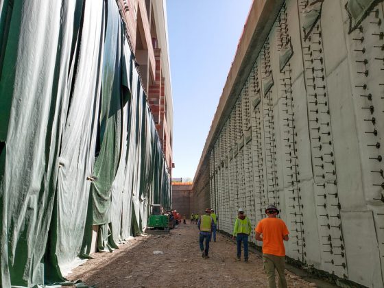 Seven construction workers wearing safety gear examine the shoring wall site at the bottom of the trench.