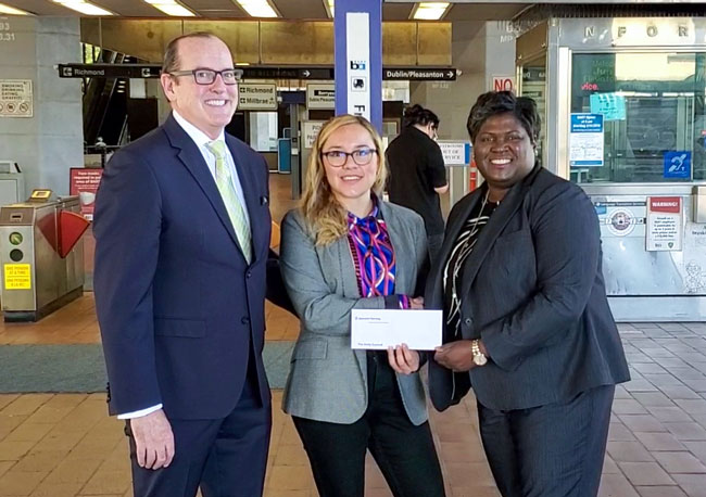 A man and a woman hand a check to a woman as part of a community involvement event.