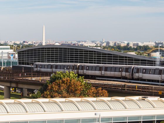 Train running along track with airport building and Washington Monument in background.