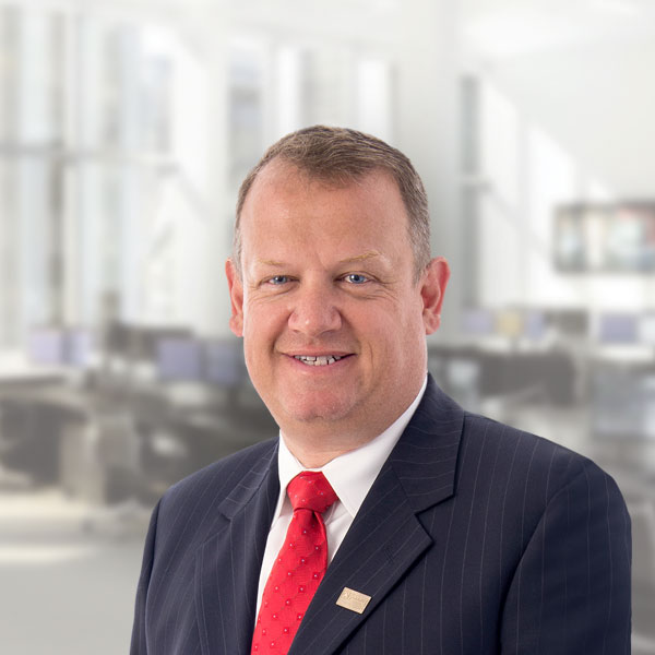 A man in a dark blue with with a white shirt and red tie smiling for the camera.