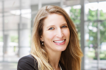 A professional woman wearing a black top and string of pearls smiles for a headshot.