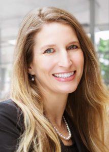 A professional woman wearing a black top and string of pearls smiles for a headshot.