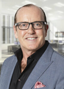 Man wearing glasses and a gray suit smiles for a portrait.