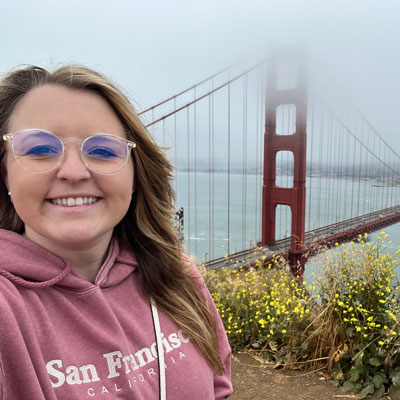 An image of a woman standing in front of the Golden Gate Bridge on a foggy day.