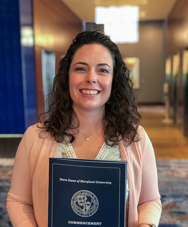 A dark curly-haired female smiles while holding a college commencement program booklet.