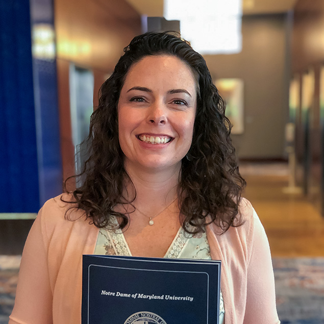 A dark curly-haired female smiles while holding a college commencement program booklet.