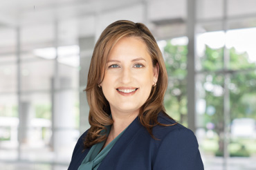 A woman in a navy blue jacket and light teal shirt smiling for the camera.