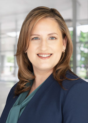 A woman in a navy blue jacket and light teal shirt smiling for the camera.