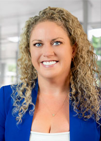 A woman poses for a professional headshot. She is smiling and wearing a white blouse and a royal blue jacket.