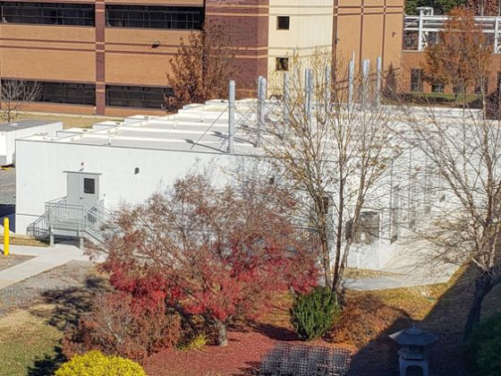 Single story white modular building with a gray door next to a multi-story tan and brick building.