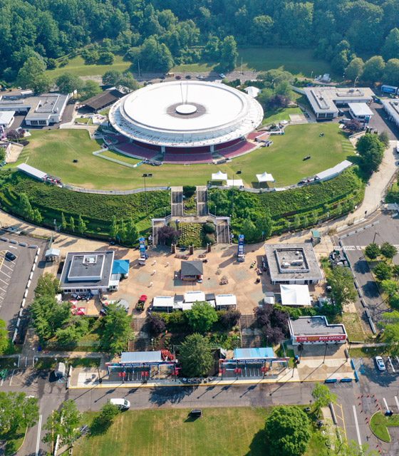 An aerial view of the circular PNC Bank Arts Center on a sunny day shows the historic open-air amphitheater and the renovated north and south plazas.