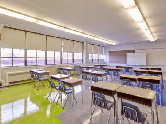 Anna Pratt Elementary School classroom with bright overhead lights and windows. Desks sit on the shiny floors that have green, white, and blue tiles.