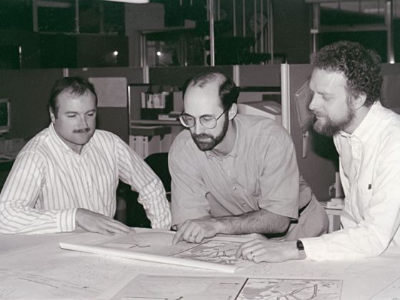 A black and white photo of Dave and two of his co-workers collaborating around a project map in 1994.