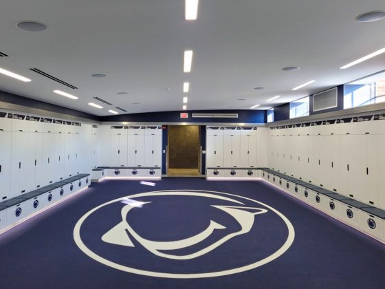 Penn State wrestling team’s locker room has white lockers with blue Nittany Lion logos. The blue floor has a large white logo in the center.