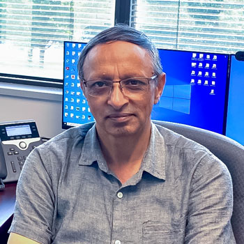 Qasir sitting at a desk in his office with computer monitors in the background.