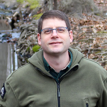 Rob outside in the woods smiling for the camera.