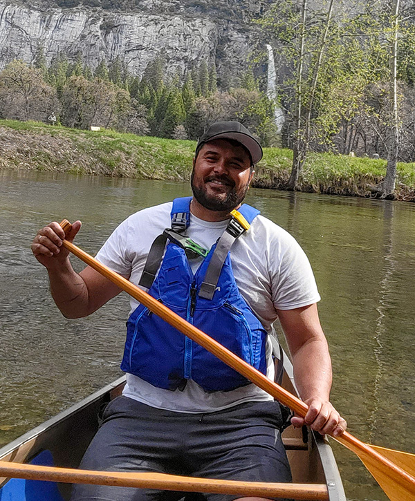 Jonny sitting in a canoe on a river with mountains and a waterfall in the background.