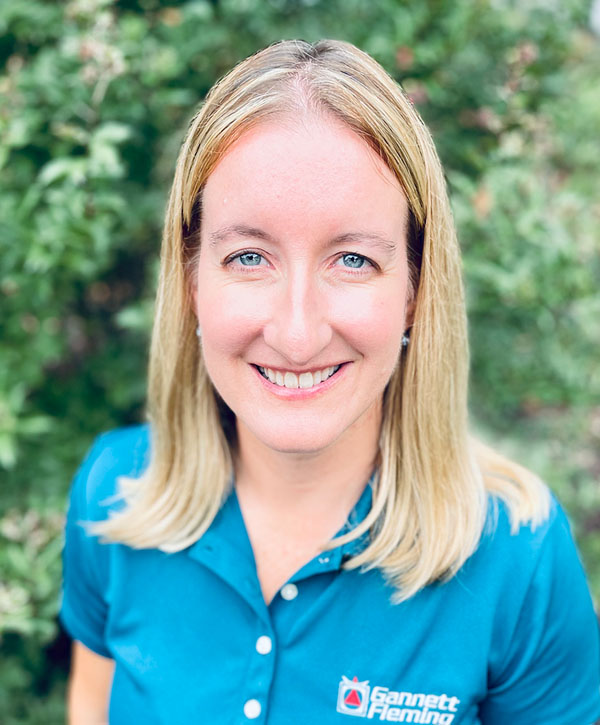 Wearing a blue shirt and standing outside, Watershed planning expert Kate Sharpe stands smiling.