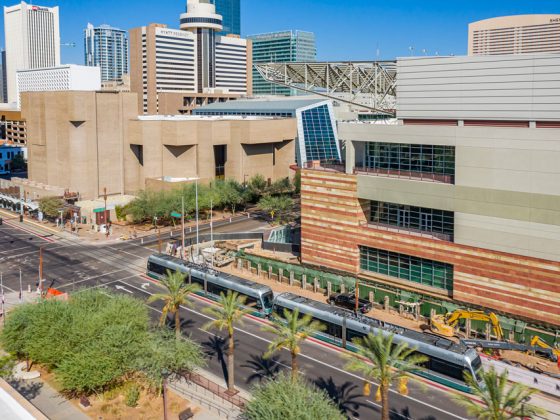 A gray light rail train running beside the Phoenix Convention Center shoring wall project site on a clear day.