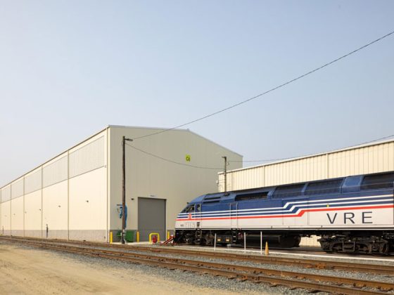 The outside of a large, tan-colored building with rail tracks and a locomotive.