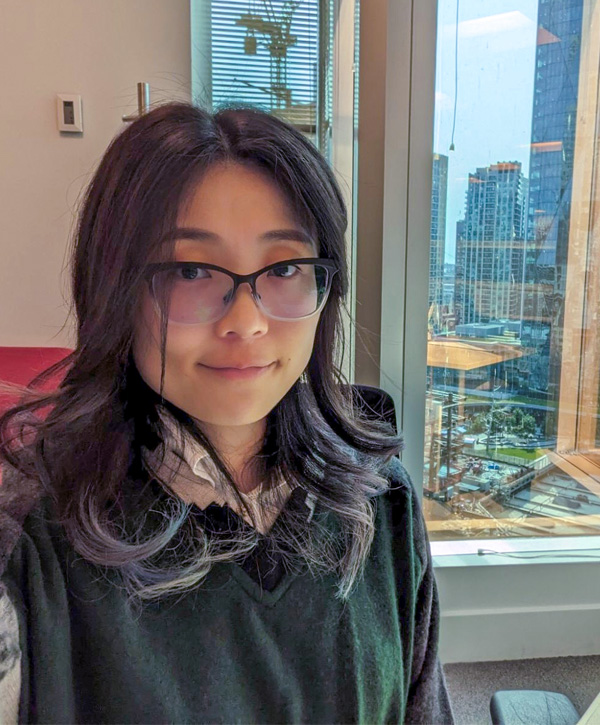 A woman posed in front of an open window, showing a cityscape.