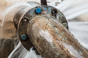 High-pressure water leak spurting from a metal pipe.