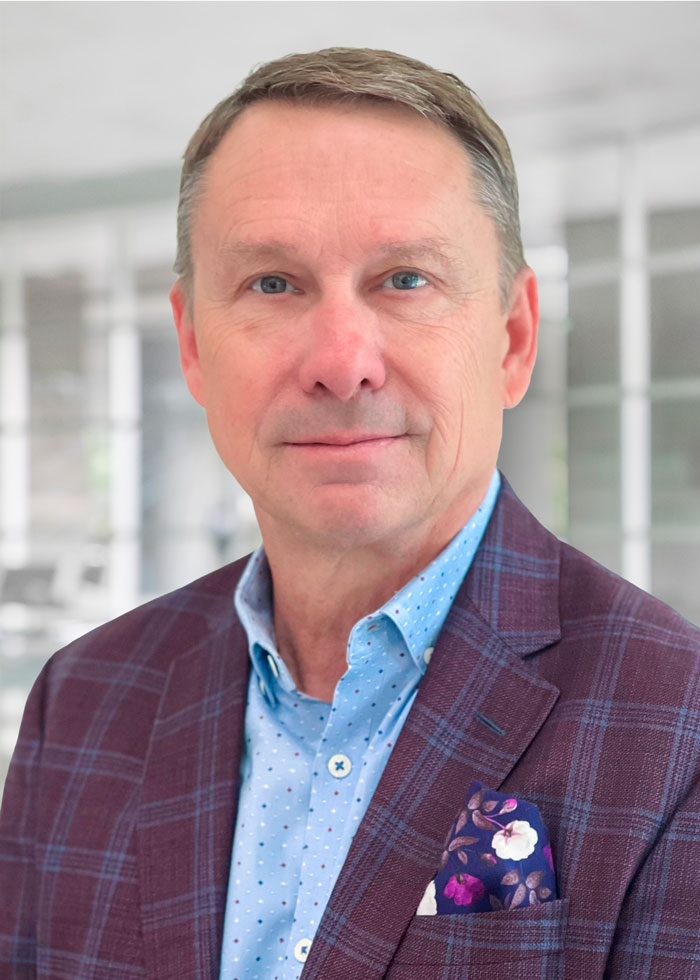 A businessman wearing a plum-colored sports coat with a floral pocket square poses for a professional headshot.