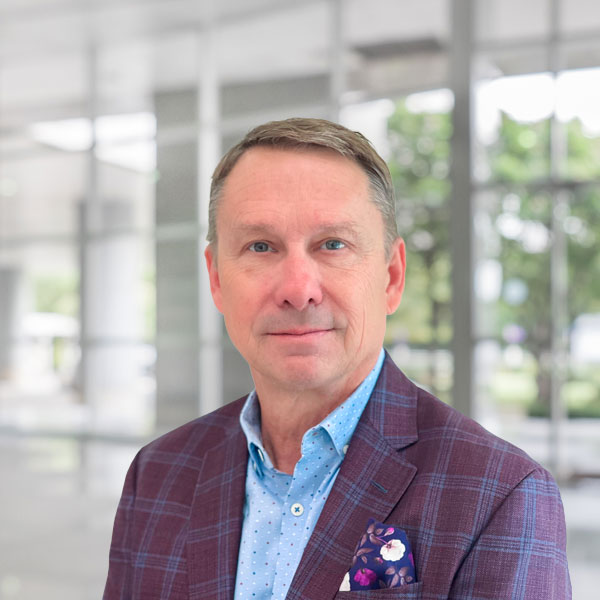 A businessman wearing a plum-colored sports coat with a floral pocket square poses for a professional headshot.