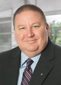 A man wearing a dark suit with a light green shirt and striped tie smiling for the camera.