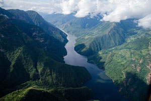 A photograph taken from above a mountain range with a river running through it and clouds in the upper right-hand corner